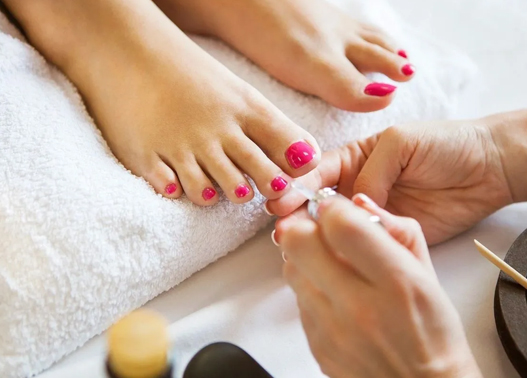 A person getting their feet painted with pink nail polish.