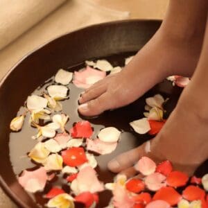 A person 's feet in a bowl of water with petals.