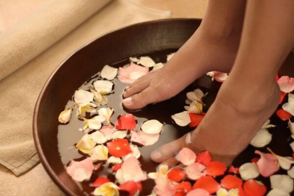 A person 's feet in a bowl of water with petals.